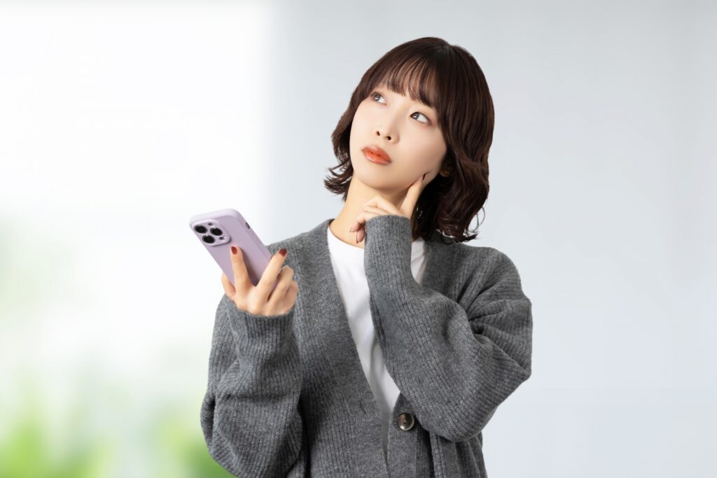 スマホを手に持って考える女性