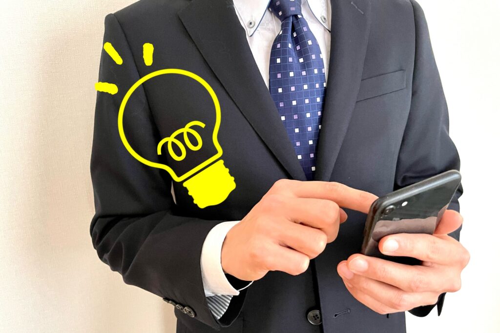 スマホを持つスーツ姿の男性。ひらめきのサイン