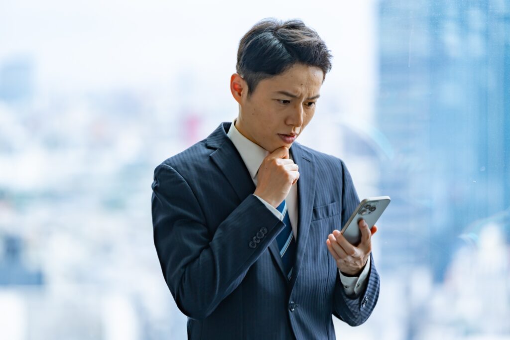 スマホ画面を見て悩む男性