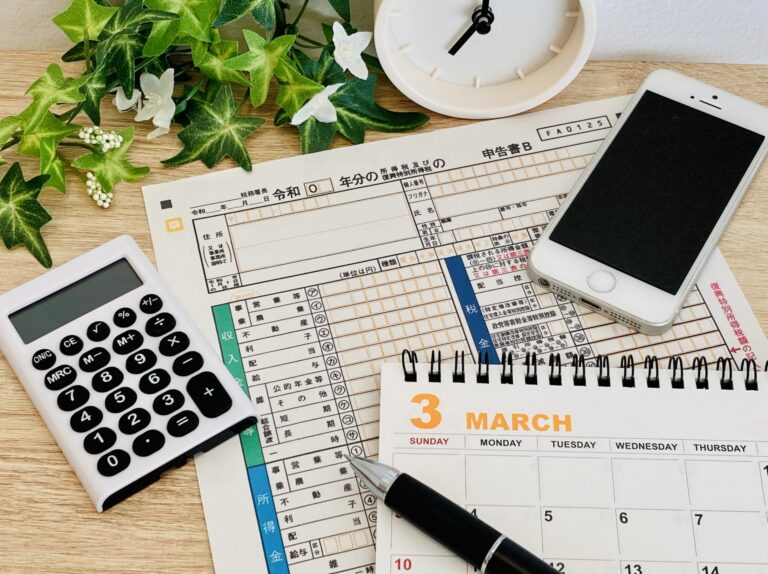 確定申告書と電卓、スマホとカレンダーが置かれた机